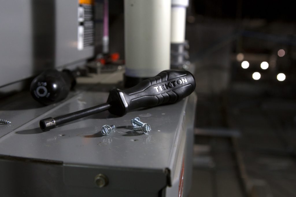 A black screwdriver sits on an HVAC unit that is being repaired.