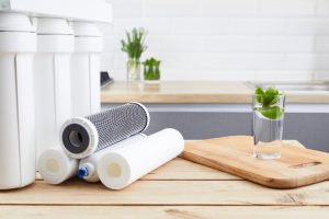 A glass of clean water with an osmosis filter and cartridges on a wooden table in a kitchen interior.